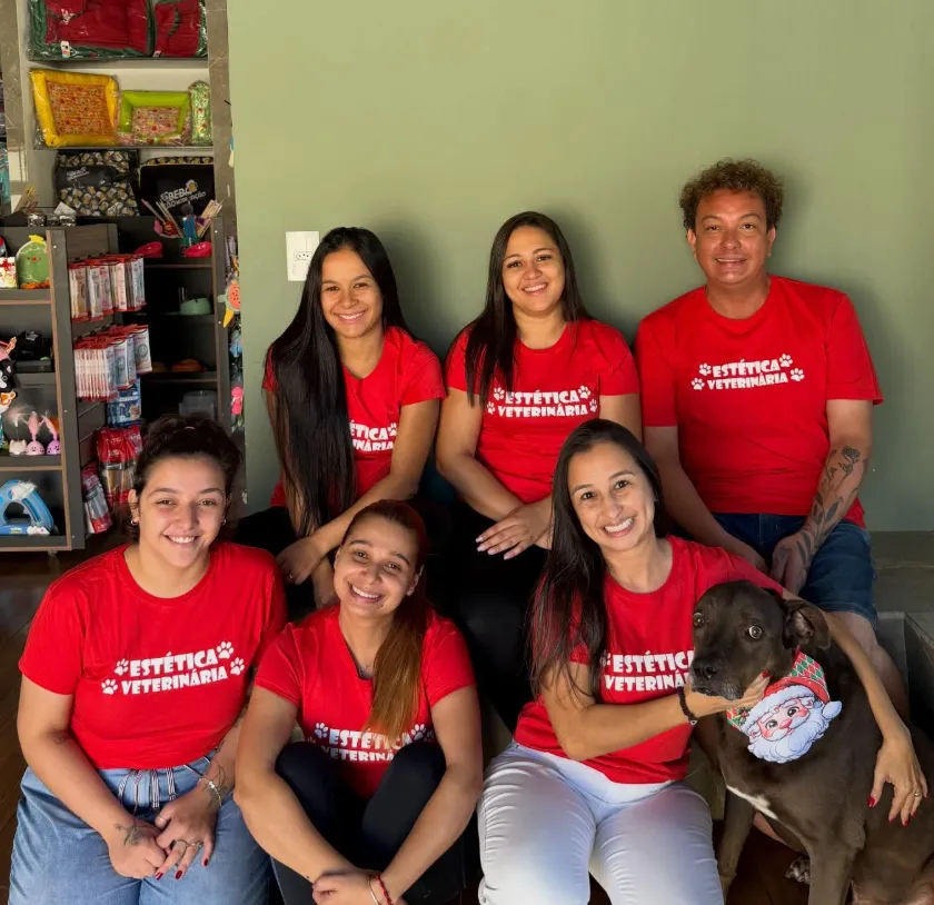 Equipe da Estética Veterinária reunida na loja, de camiseta vermelha da clínica, com um cão no colo